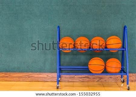 Basketballs stored in a blue metal storage rack along a blue green wall on a gym floor. Copy space.