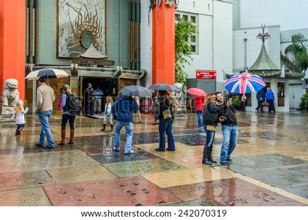 HOLLYWOOD, CA - DEC 12: Tourists standing in rain on movie star handprints on forecourt of TCL Chinese Theatre on Walk of Fame on Hollywood Boulevard, Hollywood, Los Angeles, California, Dec 12, 2014.
