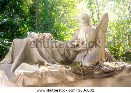 An angel sculpture praying on a tomb in a cemetery.