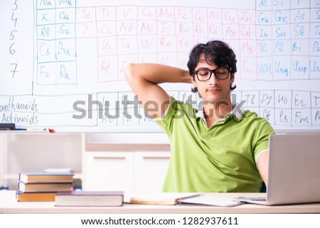 Young male student chemist in front of periodic table