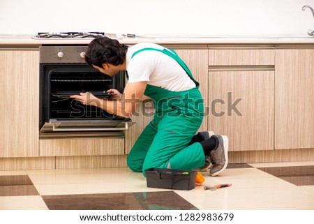 Young contractor repairing oven in kitchen