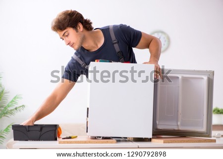 Young handsome contractor repairing fridge