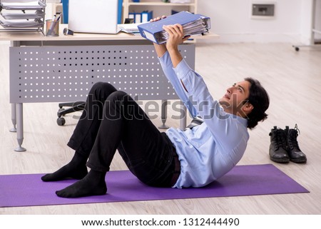 Young handsome male employee doing exercises in the office