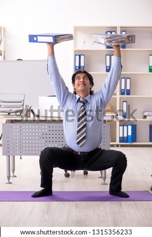Young handsome male employee doing exercises in the office