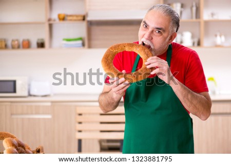 Old male baker eating in the kitchen