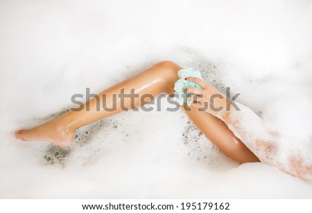 Woman in bath washing leg in bathtub with a lot of bubble bath foam. Leg of beautiful young woman in bath in bathroom.