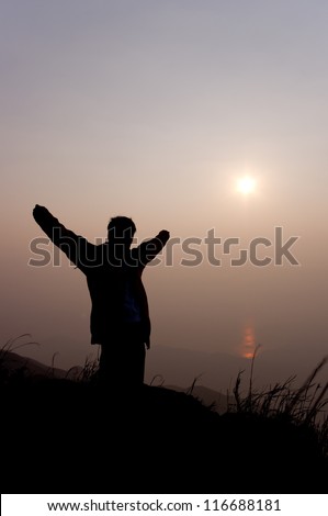 silhouette of a young man standing on the mountain with both hands raise up at sunrise