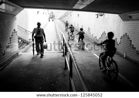 silhouette of cycling kids and father and an old walking man in the end of tunnel with back light in hong kong street