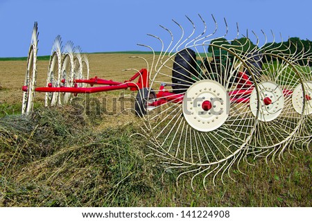 Raking Hay:  Wheels made of heavy wire spokes, pulled by a tractor, gather furrows of cut hay in preparation for baling.