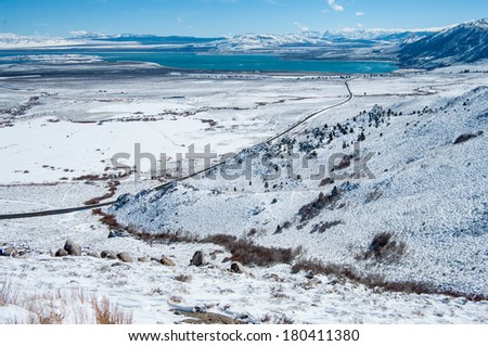 California Mountain Highway in Winter:  A scenic California highway crosses a snowy valley toward a distant lake in the Sierra Nevada Mountains near Yosemite National Park.