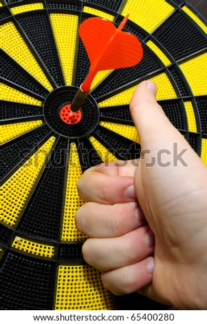 Male hand showing thumbs up with bulls eye on dart game board