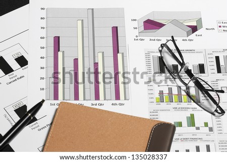 business financial chart analysis with pen eyeglasses & notebook on black table