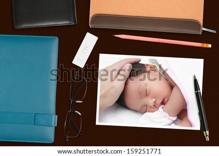 baby photo & pregnancy test with stationery on the desk