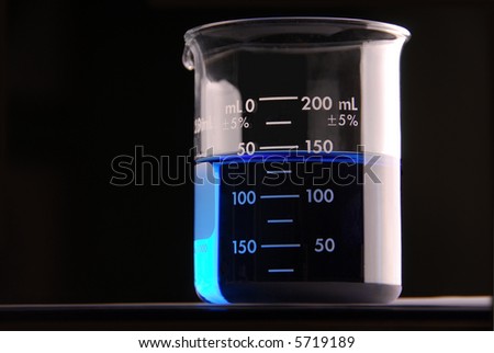A beaker in a lab with a blue liquid, black background.