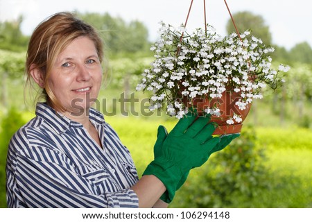 Mature woman check hanging basket with some white flower in her garden