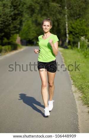 Young attractive female in green fitness outfit run on the side of the road
