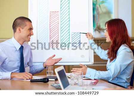 Two young colleagues argue over the graph displayed on the flip chart, conference room shoot