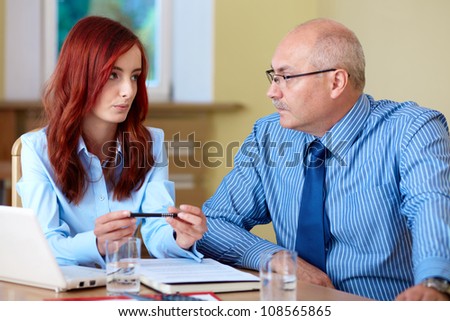 Senior businessman with young redhead female colleague discuss something