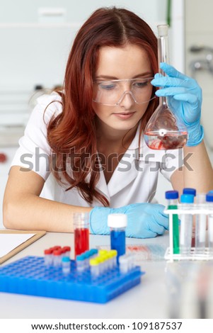 Young lab technician holds tube with red liquid, lab shoot