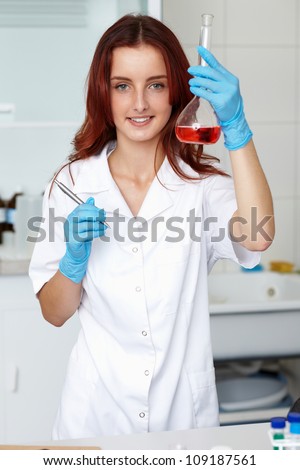 Young lab technician holds tube with red liquid, lab shoot