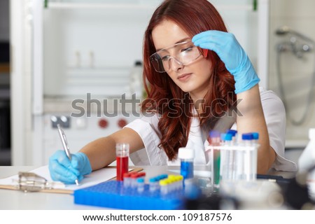 Young female lab technician works on some samples and make notes on her clipboard