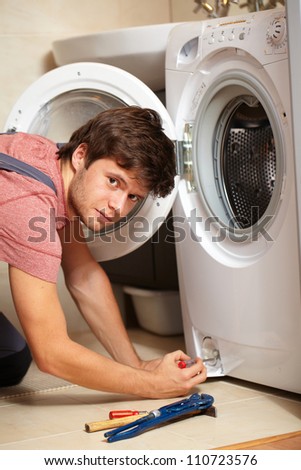 Young attractive worker in uniform fixing washing machine, background