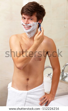 Young handsome attractive happy smiling guy with a towel shave his beard