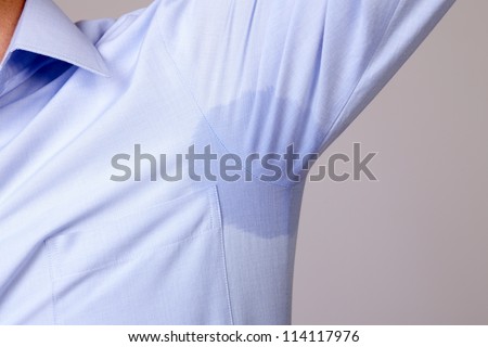 Man with hyperhidrosis sweating very badly under armpit in blue shirt, isolated on grey
