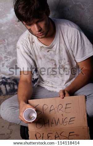 Dirty young homeless guy asking for help and spare change, sitting on a street