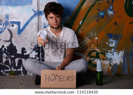 Dirty young homeless guy asking for help, sitting on a street