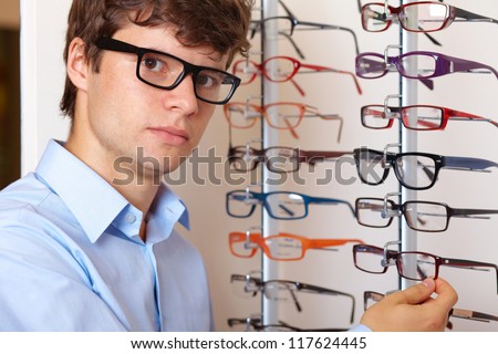 Young attractive smiling man at optician with glasses, background in optician shop