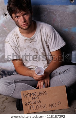 Dirty young homeless and jobless guy asking for help sitting on a street