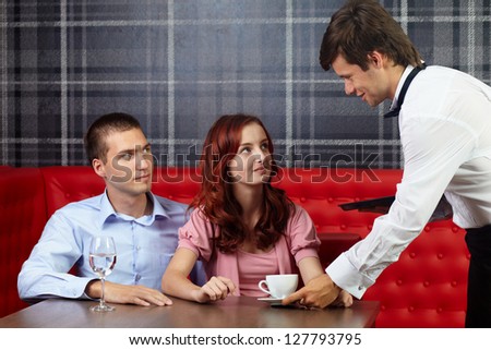 Young attractive couple sitting in restaurant and talking to handsome waiter