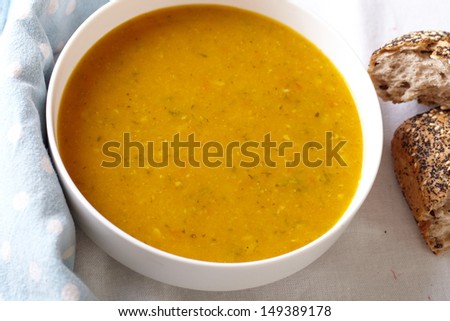 Bowl of vegetable soup with bread on side, placed on white table cloth