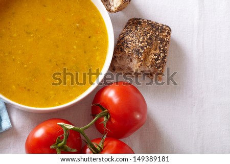 Bowl of vegetable soup with tomato and bread on side, placed on white table cloth