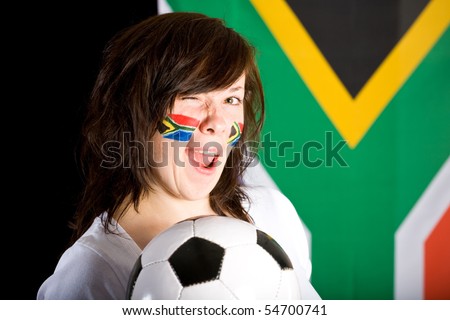 happy young soccer supporter, flags on her cheeks, holds football ball, south africa flag as background