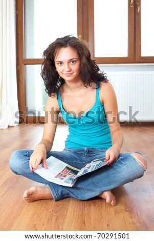 young and attractive female sits on wooden floor and read magazine, catalogue