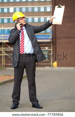young architect, inspector talk over his mobile phone, outdoor shoot with blurred office building as background