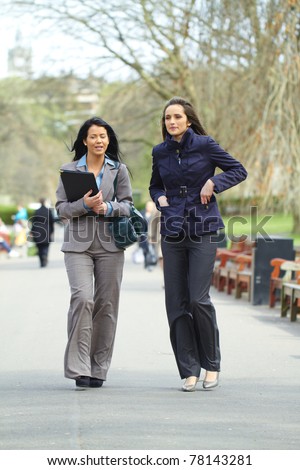 two attractive businesswoman walk in the park, both wear shirt and suit, elegant look, outdoor shoot