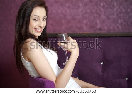 young attractive female holds wine glass, purple wall as background, sits on high chair at the bar, night out concept