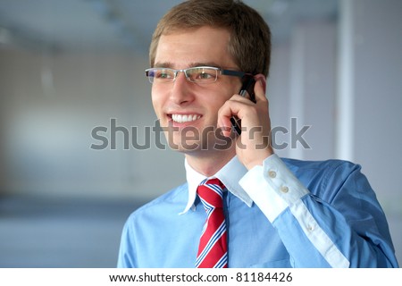 young confident businessman in blue shirt and red tie talks over mobile phone in his office
