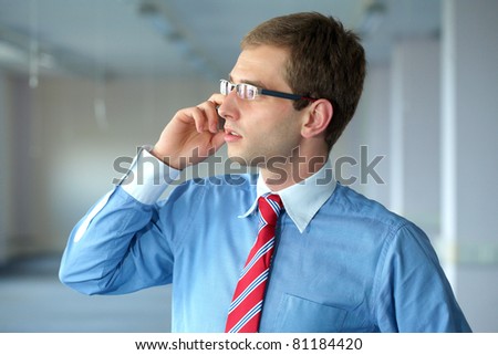 young confident businessman in blue shirt and red tie talks over mobile phone in his office