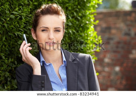 young businesswoman holds her mobile, outdoor shoot with blurred red wall as part of background, can be used as copy space