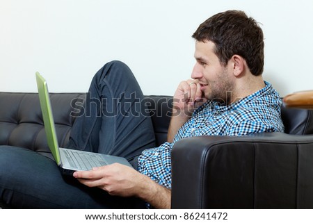 Young man sits on sofa and works on his laptop computer