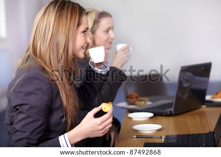 Two businesswoman sitting at conference table have a break during meeting