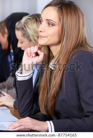 Young attractive businesswoman sitting at conference table with more people at background working on some paperwork