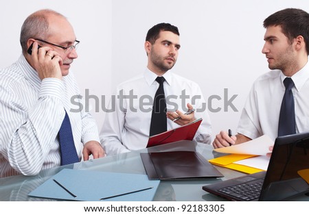 three businessman, one mature and two young ones sitting at table during meeting