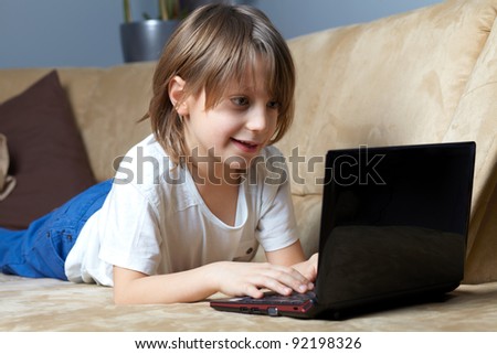 6 year old boy lying on the sofa and using his small laptop for internet or games