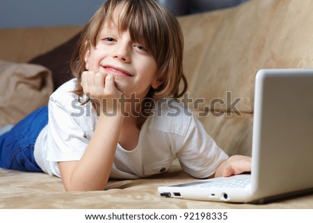 6 year old boy lying on the sofa and using his small laptop for internet or games