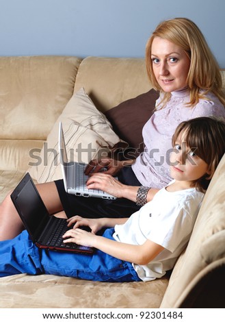 Mother and her young son sit on the sofa and work on small netbook computers